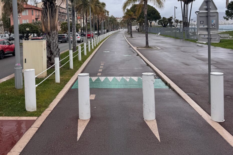 Photo de la piste cyclable de la Promenade des Anglais avec deux poteaux anti-intrustion installés sur la piste, divisant celle-ci en trois passages étroits.
