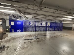 Vu d'ensemble du local vélo sécurisé à l'intérieur du parking Indigo Arénas Aéroport à Nice. Le local est clôturé par une frille bleue. L'accès est contrôlé par un boîtier de lecture de badge pour une sécurité renforcée.