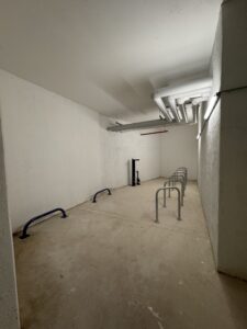 Intérieur du local vélo Indigo Joia Méridia à Nice. L'espace spacieux comprend des arceaux gris pour vélos classiques et des emplacements spécifiques au sol pour vélos cargos. Une station de services avec pompe de gonflage et outillage de réparation est à disposition des usagers.