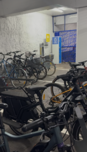 Vue intérieure du local vélo sécurisé Saleya (Indigo) à Nice. On y voit des arceaux métalliques gris permettant d'attacher plusieurs vélos par le cadre. Au fond, une station de gonflage et des casiers (lockers) numérotés sont disponibles pour l'entretien et le rangement de l'équipement.