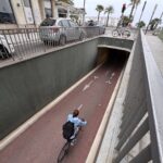 Une cycliste en pull bleu clair roule sur une piste cyclable rouge menant au mini-tunnel de la rue du Congrès.