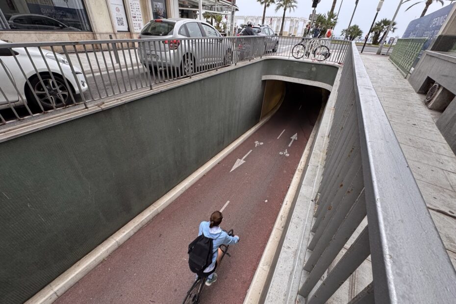 Une cycliste en pull bleu clair roule sur une piste cyclable rouge menant au mini-tunnel de la rue du Congrès.